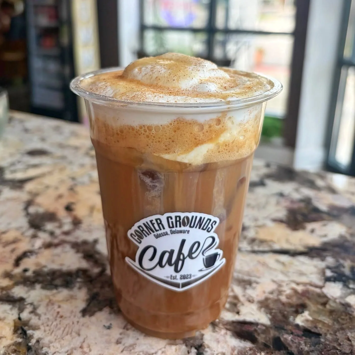 Iced latte with the Corner Grounds Café logo and a cloud of cold foam